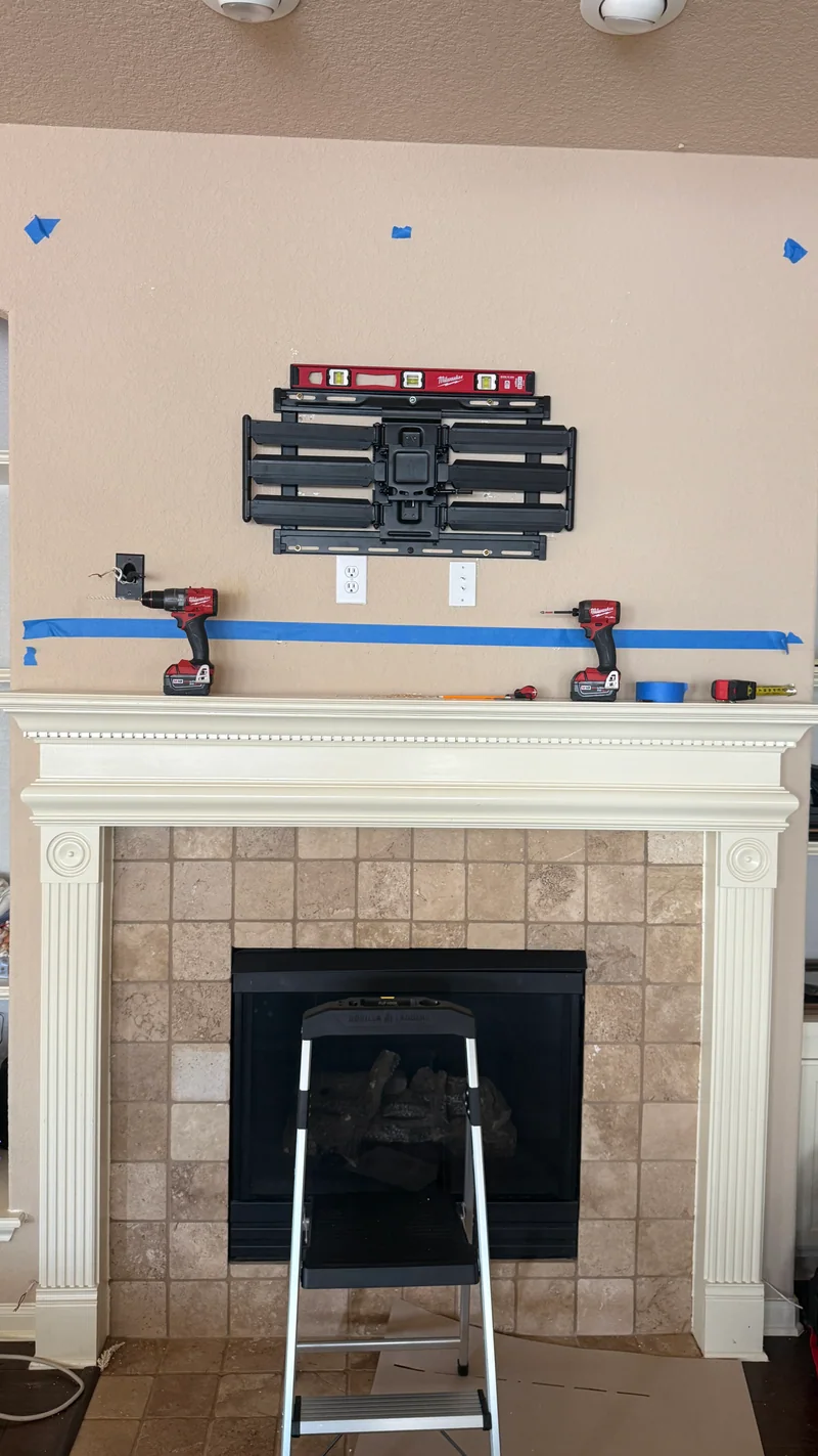 Bracket, level, painter’s tape and installation tools above a fireplace
