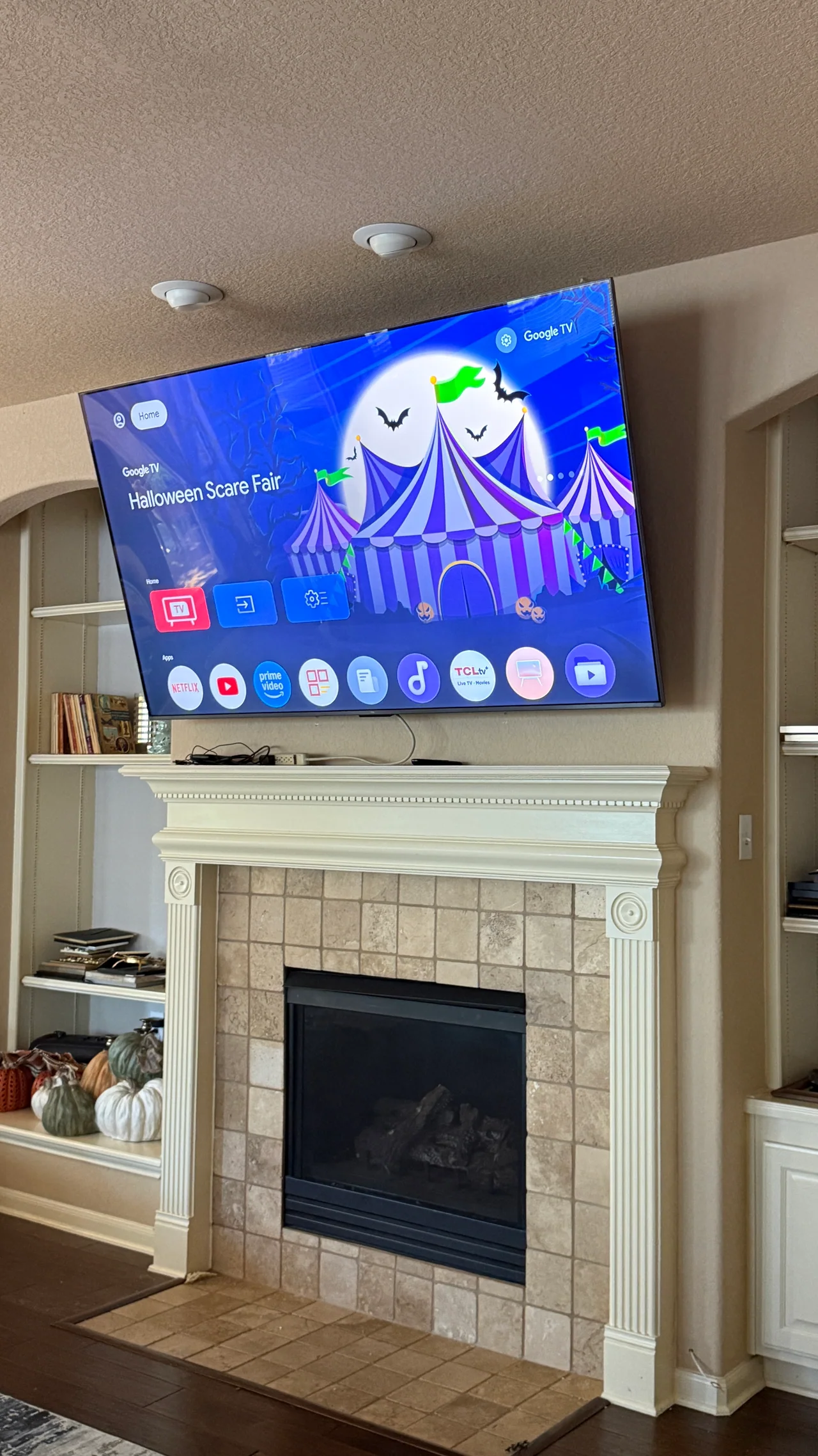 TV installed above a fireplace with the screen on; visible cables rest on the mantel.