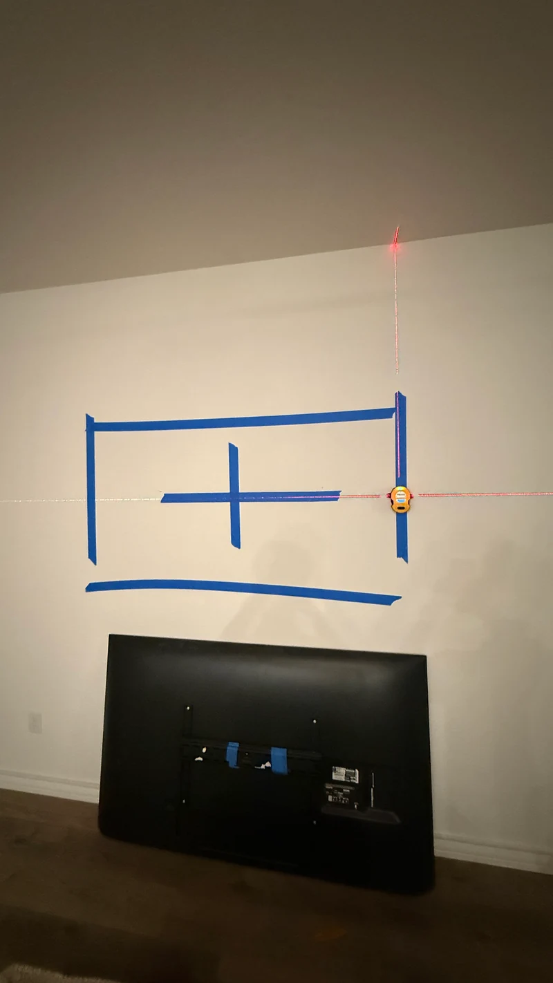 TV placement outlined with painter’s tape and a laser reference before mounting