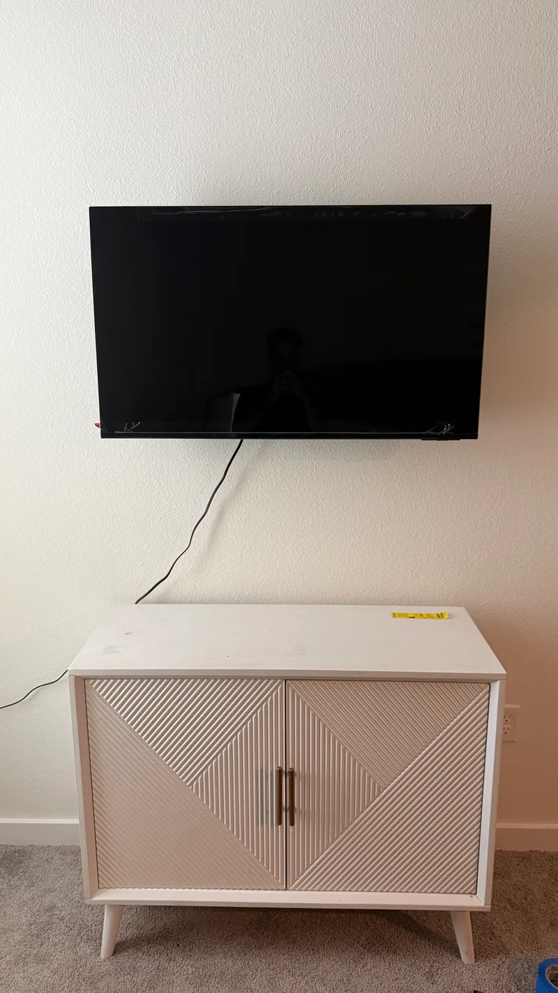 A wall-mounted TV above a white cabinet, with a visible cable running toward the left.