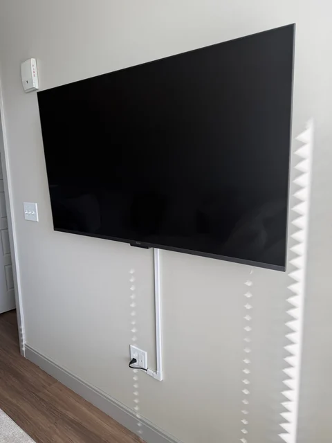 A white cable cover runs down the wall from the TV toward the existing outlet.
