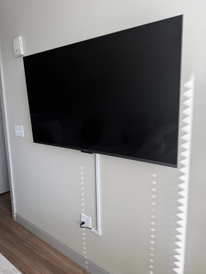 Wall-mounted TV with a white surface cable cover leading to the outlet