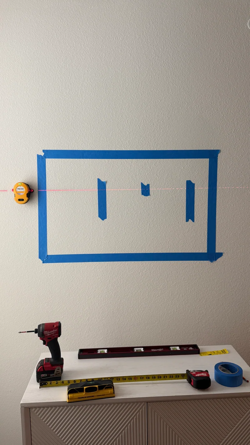 Painter’s tape marks a proposed screen position above the cabinet, with a laser reference and tools below.